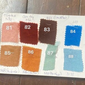May include: A colour swatch card displaying nine fabric samples in different shades. The samples are numbered 81 to 88, with Vietnamese text. Colours include pink, red, brown, blue, orange, and green.