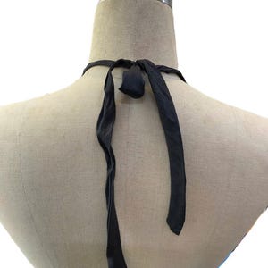 May include: A black halter top with long, flowing ties. The ties are knotted at the back of the neck. The top is displayed on a mannequin.