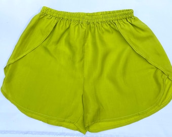 Pode incluir: Calções verde-limão brilhantes com cós elástico. Os calções têm um design envolvente, com painéis de tecido que se sobrepõem na frente. Feitos de um material leve e fluido, perfeitos para o clima quente.