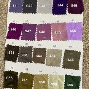 May include: A fabric colour swatch card showing a variety of shades. The card presents a spectrum of colours, including purples, greens, and neutral tones. Each fabric square is labelled with a number, for colour selection reference.