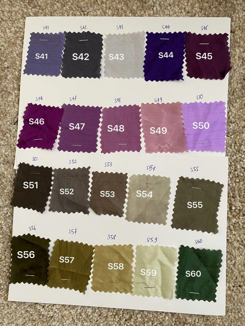 May include: A fabric colour swatch card showing a variety of shades. The card presents a spectrum of colours, including purples, greens, and neutral tones. Each fabric square is labelled with a number, for colour selection reference.