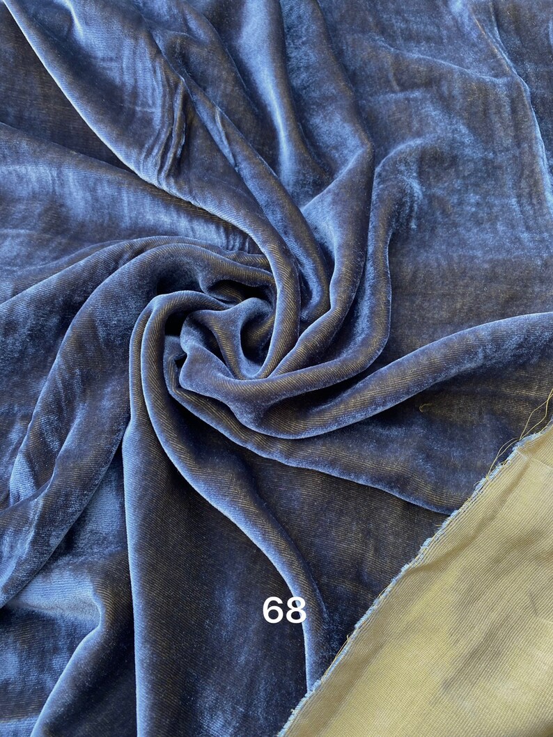 May include: A close-up of a swatch of navy blue velvet fabric. The fabric is draped and folded, creating shadows and highlights that emphasize its texture. The number "68" is printed in white on the fabric. The reverse side of the fabric is a light olive green.