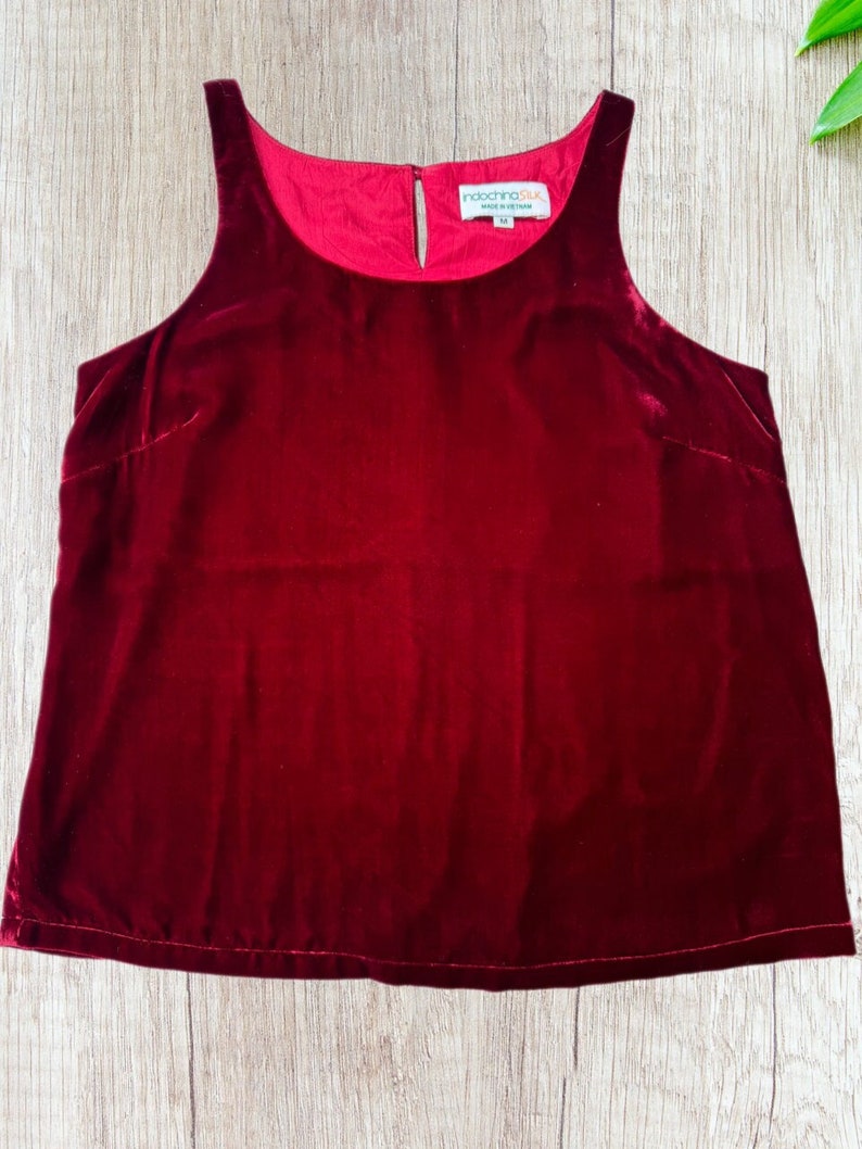 May include: A sleeveless, burgundy velvet top with a scoop neckline and a keyhole detail at the back. The top has a smooth, luxurious texture and a rich, deep red color. The tag reads "indochinaSilk".