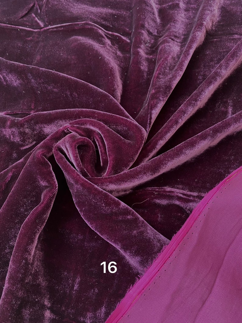May include: A close-up of a deep purple velvet fabric with a soft, lustrous texture. The fabric is draped and folded, revealing highlights and shadows. The number "16" is printed in white on the fabric. A contrasting magenta fabric is visible on the right side.