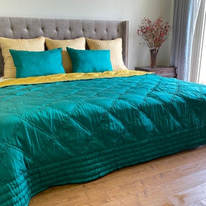 May include: A teal quilted bedspread with a diamond pattern, resting on a gray headboard with yellow and teal pillows.