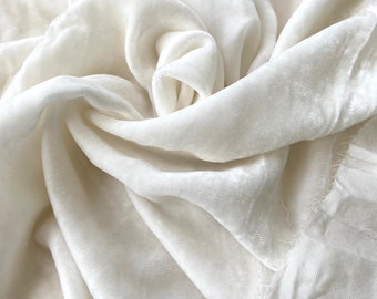 Puede incluir: Tela de terciopelo blanco con una textura suave y lisa. La tela está drapeada y doblada, mostrando su tacto lujoso.