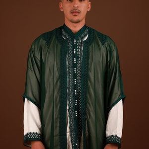 May include: A man wearing a long, dark green robe with intricate white embroidery and pearl-like embellishments. The robe has a high collar and a button closure.