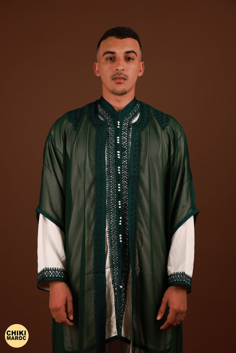 May include: A man wearing a long, dark green robe with intricate white embroidery and pearl-like embellishments. The robe has a high collar and a button closure.