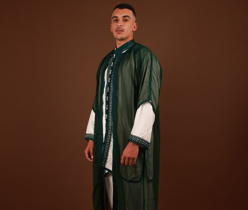 May include: A man wearing a green and white traditional robe with intricate embroidery. The robe is sheer and has a long, flowing design.