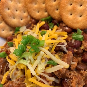 Könnte beinhalten: Eine Schüssel Chili, belegt mit geriebenem Käse, gehackten Frühlingszwiebeln und ein paar Crackern am Rand.