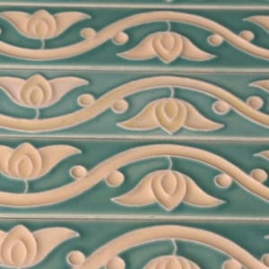 May include: A series of rectangular ceramic tiles featuring a repeating embossed pattern of cream-colored lotus flowers and curved vines set against a smooth, matte teal background. The design creates a continuous horizontal border motif.