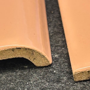 May include: Two close-up images of peach-colored ceramic tile trim pieces. The tile trim has a rounded edge and a rough, textured back.