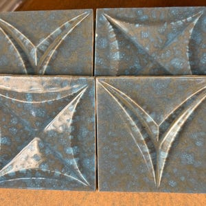 May include: Four square ceramic tiles with a blue and brown glaze. Each tile has a raised, embossed design of a stylized leaf shape.