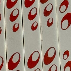 May include: A series of white vertical panels featuring a repeating pattern of red oval shapes. Each red oval contains a smaller, off-center white oval, creating a layered effect across the surface of the panels. The design is consistent.