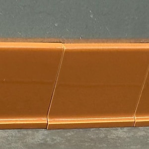 May include: A series of connected, orange-colored, rectangular pieces. Each piece has a beveled edge, creating a subtle angled design. The pieces are arranged in a linear fashion, suggesting a trim or molding element.