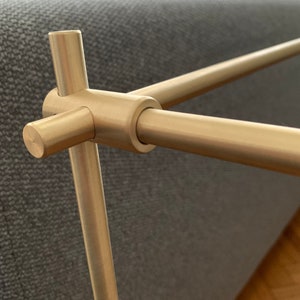 Może przedstawiać: Zbliżenie na złoty metalowy wspornik p&oacute;łki z okrągłym złączem. Wspornik wykonany jest z gładkiego, polerowanego metalu i ma prosty, nowoczesny design.