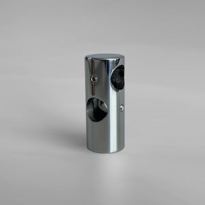 Könnte beinhalten: Ein silbernes Metallrohrfitting mit zwei seitlich eingeschnittenen Löchern. Das Fitting hat eine glatte, polierte Oberfläche.