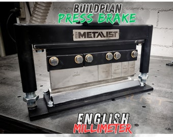 Puede incluir: Una prensa de plegado de metal negro con una cuchilla de metal plateado. La cuchilla tiene marcas para diferentes ángulos de plegado en pulgadas y milímetros. La prensa de plegado está etiquetada como "BUILDPLAN PRESS BRAKE" y "THE METALIST".