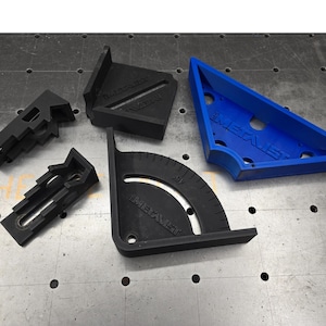 May include: Four black plastic woodworking tools, including a protractor, a corner clamp, and two L-shaped clamps. One of the L-shaped clamps is blue.