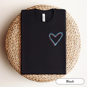 Könnte beinhalten: Schwarzes T-Shirt mit einem pinkfarbenen und blauen Herzdesign.