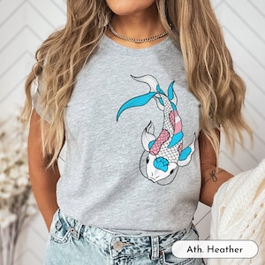 K&ouml;nnte beinhalten: Ein heidefarbenes T-Shirt mit einem blauen, rosa und wei&szlig;en Koi-Fisch-Motiv. Der Text "Ath. Heather" ist in der rechten unteren Ecke des Shirts aufgedruckt.