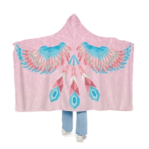 Pode incluir: Uma manta de capuz rosa com um design geométrico de asas e penas em tons de azul, rosa e branco.