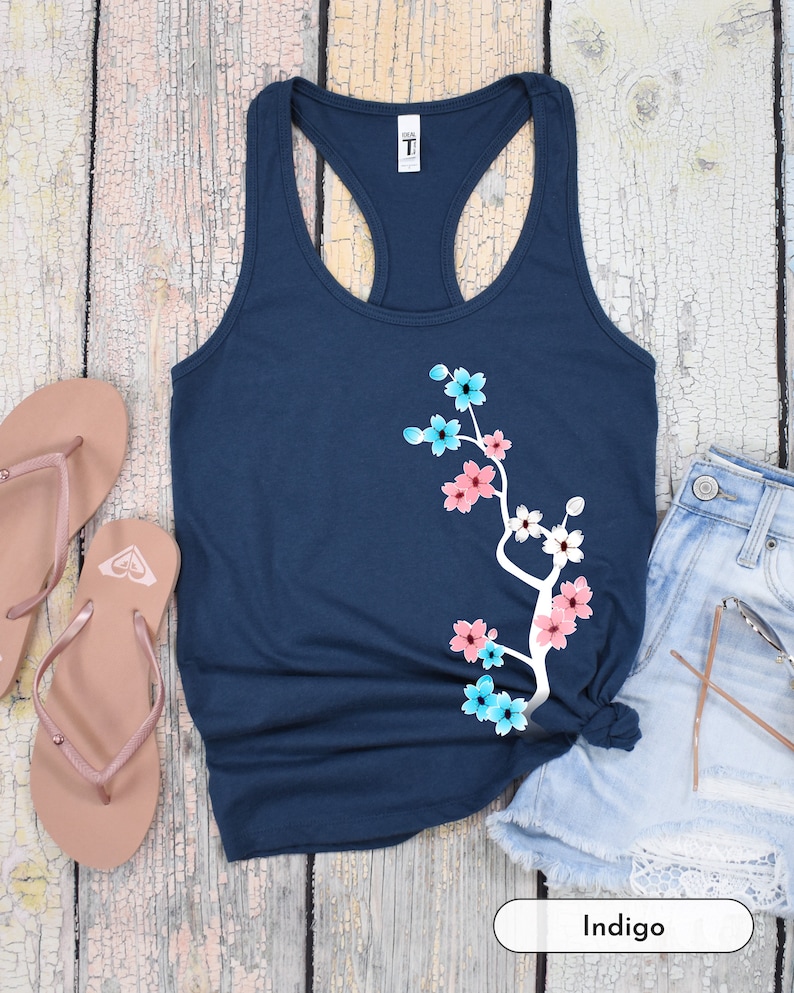 May include: A navy blue tank top with a white floral design. The design features pink, blue, and white flowers on a branch. The tank top is made of a soft, comfortable material and is perfect for everyday wear.