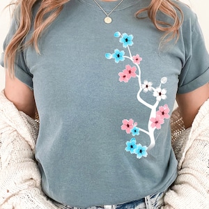 May include: A light blue t-shirt with a white floral design featuring pink and blue flowers. The flowers are arranged in a branch-like pattern. The text "Ice Blue" is visible in the bottom right corner of the image.