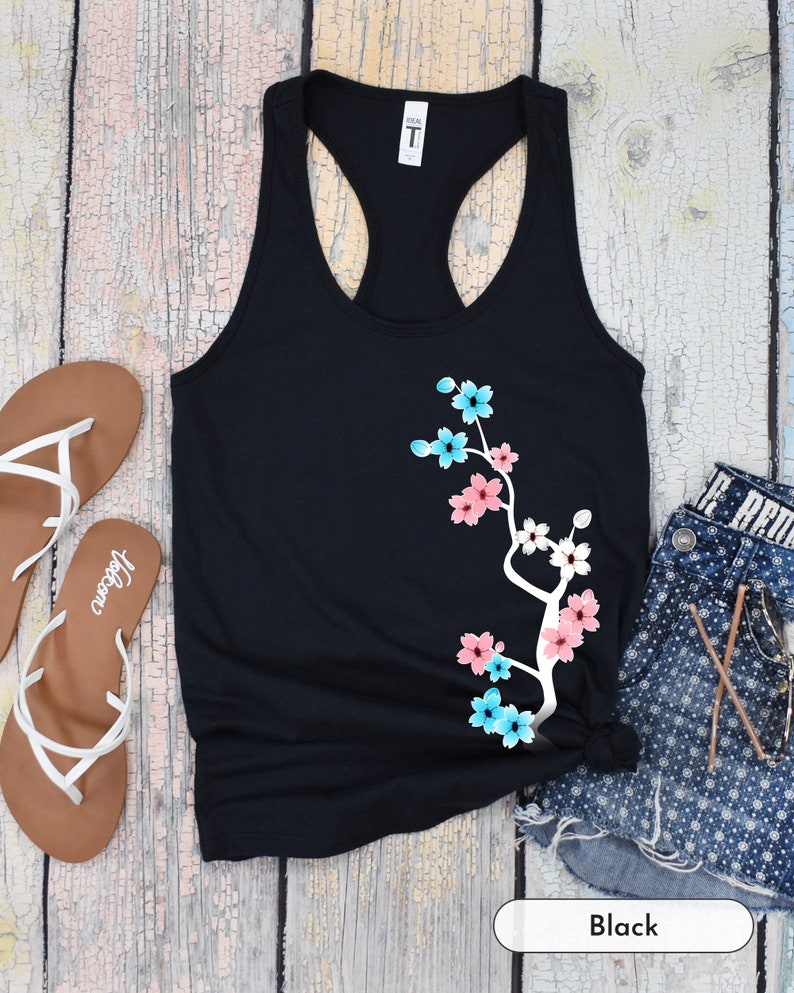 May include: Black tank top with a white branch and pink and blue flowers printed on the front. The text "Black" is printed below the tank top.