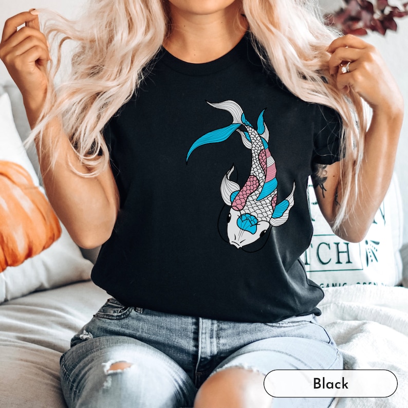 K&ouml;nnte beinhalten: Ein schwarzes T-Shirt mit einem blauen, rosa und wei&szlig;en Koi-Fisch-Motiv. Der Fisch ist stilisiert und hat ein detailliertes Design.