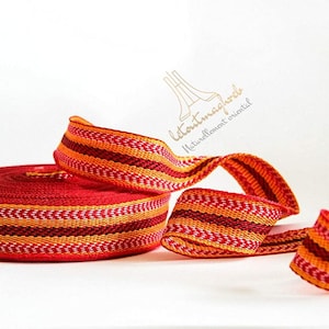 Peut inclure: Ruban tissé rayé rouge et orange avec un motif en chevron. Le ruban est enroulé et une longueur est drapé sur le rouleau.