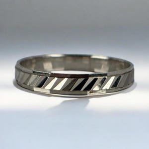 Puede incluir: Un anillo de plata con un diseño geométrico. El anillo presenta una serie de facetas rectangulares anguladas que alternan entre tonos claros y oscuros de plata. La banda tiene un perfil plano y un acabado pulido, creando una estética moderna y minimalista.