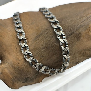 May include: A silver chain necklace with a curb link design. The links are textured with a diamond pattern.