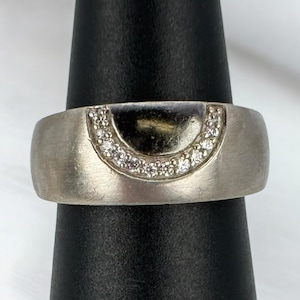 Könnte beinhalten: Ein silberner Ring mit einem halbmondförmigen Design, besetzt mit kleinen Diamanten.