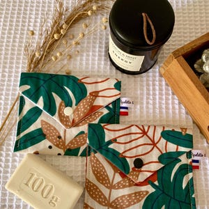 Peut inclure: Deux pochettes carrées en tissu avec une base blanche et un motif de feuilles de monstera vertes et de feuillage brun pointillé. Chaque pochette présente un rabat triangulaire avec un bouton-pression et une étiquette Pipelette & Co.