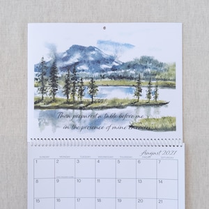 May include: A watercolour calendar page for August 2027, depicting a landscape with mountains, trees, and a lake. The text "Thou preparest a table before me in the presence of mine enemies" is shown. The calendar grid is visible.