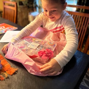 May include: A clear plastic rectangular storage container filled with various colorful play dough accessories, including small shaped cutters and decorative items. A white label on the lid features the text LIFE MAGIC HAPPY.