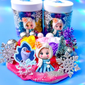 May include: Two clear jars filled with colorful slime, glitter, and small toys, including a miniature Elsa doll and Olaf from Disney's Frozen. The jars are surrounded by a pink and white slime with glitter and snowflake decorations.