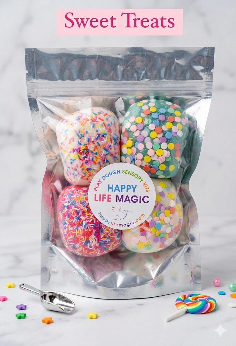 May include: A clear, resealable pouch containing four round balls of play dough in white, teal, pink, and off-white, each decorated with colourful sprinkles. A circular label reads "PLAY DOUGH SENSORY KITS HAPPY LIFE MAGIC" with a bird icon.