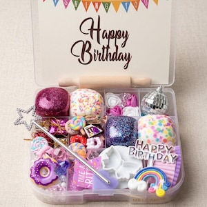 May include: A clear plastic organizer box filled with birthday-themed craft supplies, including miniature donuts, a disco ball, colorful sprinkles, a star wand, and a sign that reads WISHING YOU A HAPPY BIRTHDAY and HAPPY BIRTHDAY.