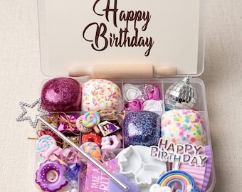 May include: A clear plastic box filled with colorful craft supplies and decorations. The box contains glittery spheres, miniature donuts, candies, and a rainbow. A card with "Happy Birthday" is visible. A small rolling pin is also included.