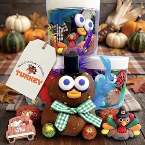 May include: A Build A Play Dough Turkey kit featuring two clear plastic containers filled with colourful dough, feathers, and googly eyes. A brown dough turkey figure with a black top hat and green gingham bow sits in front with a tag.