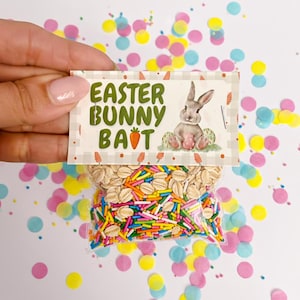 Könnte beinhalten: Ein kleiner Beutel mit Haferflocken und bunten Streuseln, mit einer Karte mit der Aufschrift "Easter Bunny Bait" und einer Hasenillustration. Der Hintergrund ist mit bunten Konfetti dekoriert.