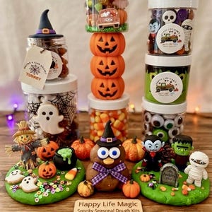 May include: A collection of Halloween-themed sensory dough kits featuring clear plastic jars filled with candy corn, plastic eyeballs, and small figurines. Includes a scarecrow, ghost, vampire, mummy, and Frankenstein figures on green dough bases.