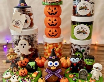 May include: A collection of Halloween-themed sensory dough kits featuring clear plastic jars filled with candy corn, plastic eyeballs, and small figurines. Includes a scarecrow, ghost, vampire, mummy, and Frankenstein figures on green dough bases.
