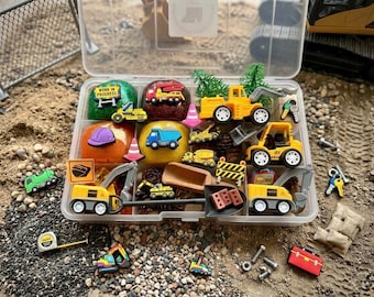 May include: A clear plastic storage container filled with construction-themed sensory play items, including yellow toy excavators, dump trucks, miniature traffic cones, signs reading Work in Progress, colorful dough balls, small plastic trees, and metal bolts.
