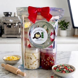 May include: A clear iridescent pouch topped with a red bow containing a sensory dough play kit. The label reads Happy Life Magic Moka o Pizza Sensory Dough Play Kit. Inside are two jars of dough with gold glitter, a metal tin, and small accessories.