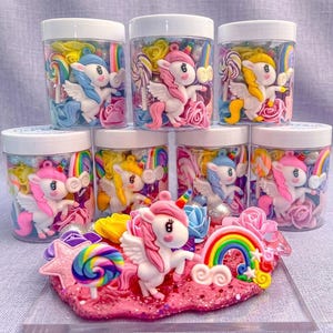 Pode incluir: Uma coleção de potes de plástico transparente cheios de decorações coloridas com tema de unicórnio. Cada pote contém uma figura de unicórnio em miniatura, arco-íris, pirulitos e flores. Uma peça de exibição maior com um unicórnio, arco-íris e outras decorações está em primeiro plano.
