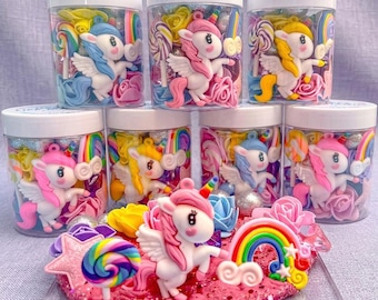May include: A collection of clear plastic jars filled with colorful unicorn-themed decorations. Each jar contains a miniature unicorn figurine, rainbows, lollipops, and flowers. A larger display piece with a unicorn, rainbow, and other decorations is in the foreground.
