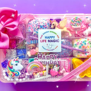 May include: A rectangular pink plastic storage container filled with various colorful sensory play items, including a unicorn figurine, a rainbow charm, a yellow butterfly mold, and a Happy Birthday sign. A large pink bow is attached to the top left.